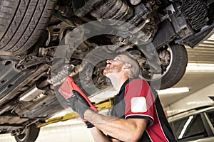 Handsome mechanic based on car in auto repair shop with tablet on hand