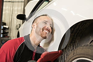 Handsome mechanic based on car in auto repair shop with tablet on hand