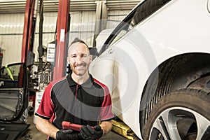 Handsome mechanic based on car in auto repair shop with tablet on hand