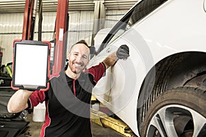 Handsome mechanic based on car in auto repair shop with tablet on hand