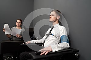 Woman testing man with polygraph in grey room.