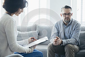 Man sitting on a gray sofa during a meeting with a psychotherapist photo