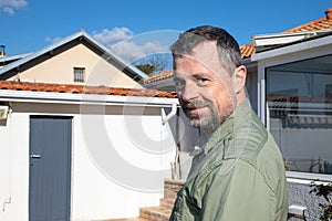 handsome middle age caucasian man smiling in garden near wood hut house