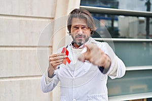 Handsome middle age doctor man holding support red ribbon pointing with finger to the camera and to you, confident gesture looking