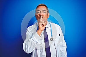 Handsome middle age doctor man wearing stethoscope over isolated blue background asking to be quiet with finger on lips