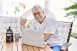 Handsome middle age hispanic man with grey hair and glasses working using computer laptop at home