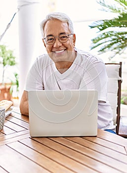 Handsome middle age hispanic man with grey hair and glasses working using computer laptop at home