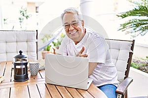 Handsome middle age hispanic man with grey hair and glasses working using computer laptop at home