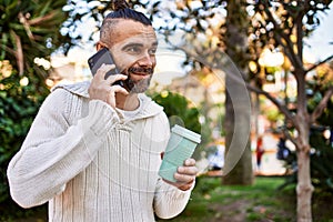 Handsome middle age man with beard standing happy and confident outdoors having a conversation speaking on the phone