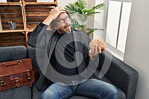 Handsome middle age man at consultation office holding brain stressed and frustrated with hand on head, surprised and angry face