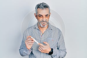 Handsome middle age man with grey hair holding glucometer device skeptic and nervous, frowning upset because of problem