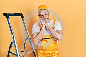 Handsome middle age man with grey hair holding ladder sleeping tired dreaming and posing with hands together while smiling with