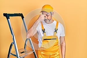 Handsome middle age man with grey hair holding ladder tired rubbing nose and eyes feeling fatigue and headache