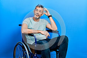 Handsome middle age man with grey hair sitting on wheelchair confuse and wondering about question