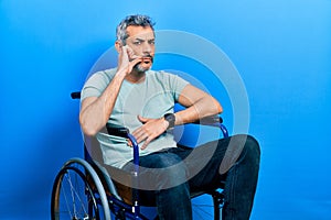 Handsome middle age man with grey hair sitting on wheelchair mouth and lips shut as zip with fingers