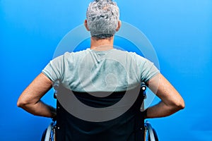 Handsome middle age man with grey hair sitting on wheelchair standing backwards looking away with arms on body