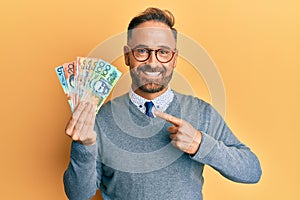 Handsome middle age man holding australian dollars smiling happy pointing with hand and finger