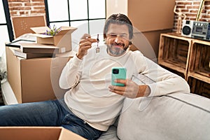 Handsome middle age man holding keys of new home doing video call smiling with a happy and cool smile on face