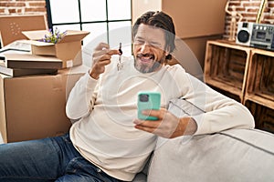 Handsome middle age man holding keys of new home doing video call winking looking at the camera with sexy expression, cheerful and