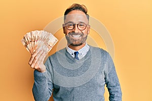 Handsome middle age man holding south african 20 rand banknotes looking positive and happy standing and smiling with a confident