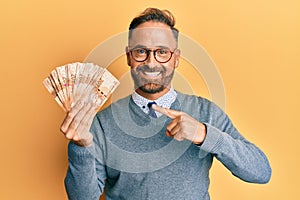 Handsome middle age man holding south african 20 rand banknotes smiling happy pointing with hand and finger