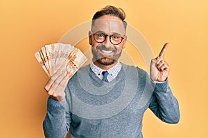Handsome middle age man holding south african 20 rand banknotes smiling happy pointing with hand and finger to the side