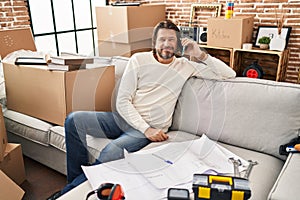 Handsome middle age man moving to a new home speaking on the phone looking positive and happy standing and smiling with a