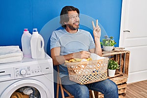 Handsome middle age man waiting for laundry smiling with happy face winking at the camera doing victory sign