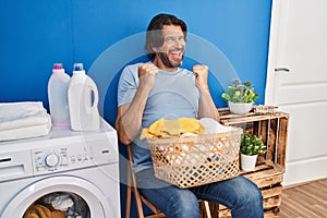 Handsome middle age man waiting for laundry very happy and excited doing winner gesture with arms raised, smiling and screaming