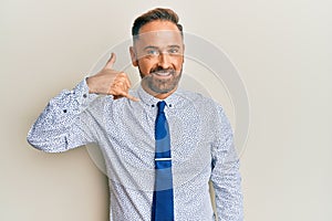 Handsome middle age man wearing business shirt and tie smiling doing phone gesture with hand and fingers like talking on the