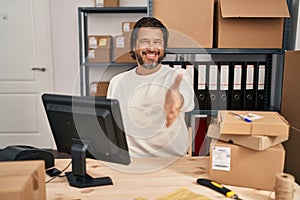 Handsome middle age man working at small business ecommerce smiling friendly offering handshake as greeting and welcoming
