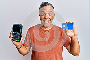 Handsome middle age mature man holding dataphone and credit card smiling and laughing hard out loud because funny crazy joke