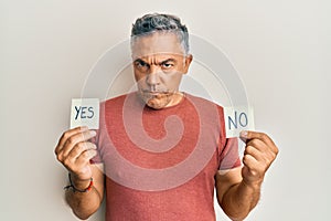 Handsome middle age mature man holding yes and no reminder skeptic and nervous, frowning upset because of problem