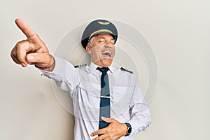 Handsome middle age mature man wearing airplane pilot uniform laughing at you, pointing finger to the camera with hand over body,