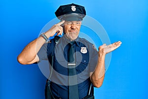 Handsome middle age mature man wearing police uniform confused and annoyed with open palm showing copy space and pointing finger