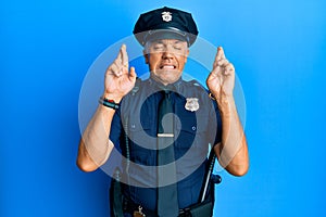 Handsome middle age mature man wearing police uniform gesturing finger crossed smiling with hope and eyes closed