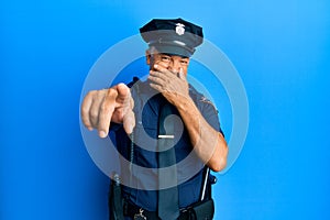 Handsome middle age mature man wearing police uniform laughing at you, pointing finger to the camera with hand over mouth, shame