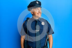 Handsome middle age mature man wearing police uniform looking away to side with smile on face, natural expression