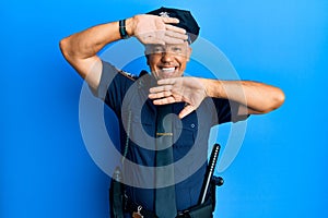 Handsome middle age mature man wearing police uniform smiling cheerful playing peek a boo with hands showing face