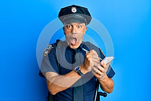 Handsome middle age mature man wearing police uniform writing a ticket afraid and shocked with surprise and amazed expression,