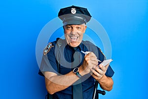 Handsome middle age mature man wearing police uniform writing a ticket smiling and laughing hard out loud because funny crazy joke