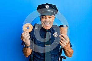 Handsome middle age mature police man eating donut and drinking coffee smiling and laughing hard out loud because funny crazy joke