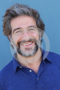 Handsome middle age Mediterranean man in a studio portrait on a blue wall background smiling