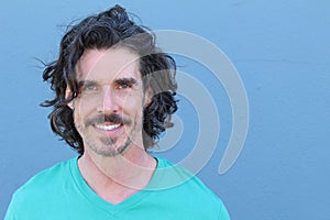 Handsome middle age Mediterranean man in a studio portrait on a blue wall background smiling with copy space