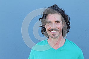 Handsome middle age Mediterranean man in a studio portrait on a blue wall background smiling with copy space on the left side