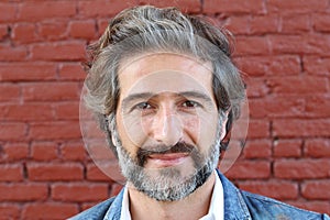 Handsome middle age Mediterranean man in a studio portrait on a red brick wall background