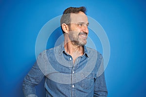 Handsome middle age senior man with grey hair over isolated blue background smiling looking to the side and staring away thinking