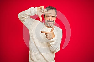 Handsome middle age senior man with grey hair over isolated red background smiling making frame with hands and fingers with happy