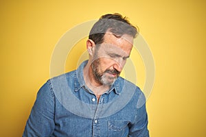 Handsome middle age senior man with grey hair over isolated yellow background with hand on stomach because indigestion, painful