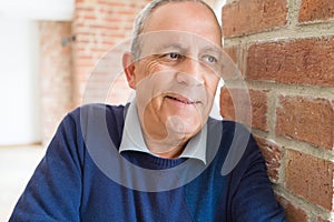 Handsome middle age senior man smiling cheerful, happy and positive leaning over bricks wall outdoors
